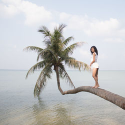 Side view of woman standing on palm tree trunk over sea