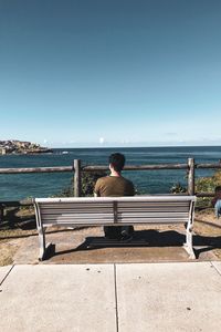 Rear view of man sitting on bench against sea