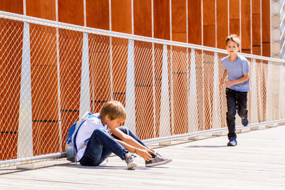 Boy photographing while friend running on footbridge in city