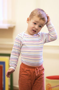 Portrait of cute boy with hand in hair standing at home