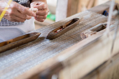 Midsection of person holding thread while standing by wooden table