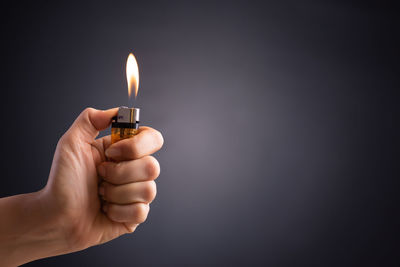 Close-up of hand holding cigarette lighter against gray background