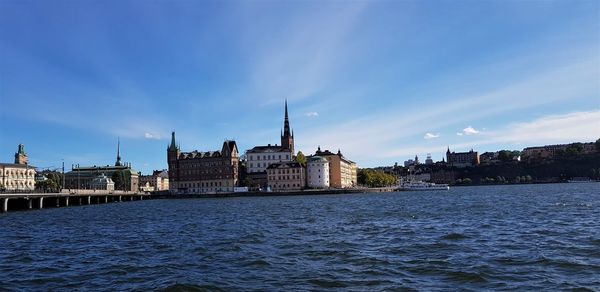 View of buildings by river against blue sky