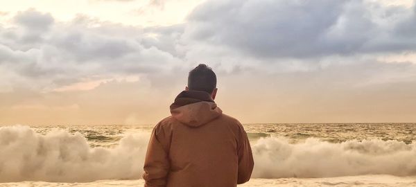 Rear view of man standing at beach against sky