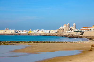 Scenic view of sea by buildings against clear blue sky