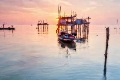 Sailboats moored in sea against sky during sunset