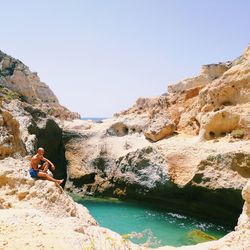 Man standing on cliff by sea against clear sky