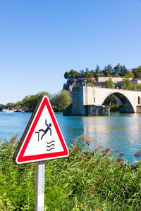 Warning sign on bridge over river against clear sky