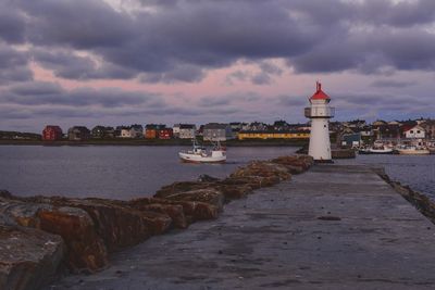Lighthouse amidst buildings by sea against sky
