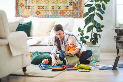 Full length of multi-tasking mother with fabric swatches and daughter working in living room at home