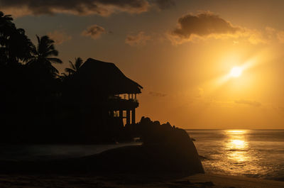 Silhouette built structure on beach against sky during sunset