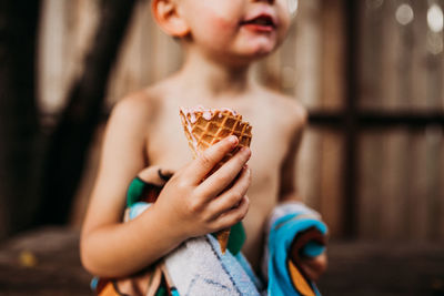 Close up of young boy holding dripping ice cream cone in summer