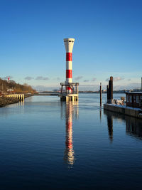 Lighthouse by sea against clear blue sky