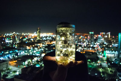 Close-up of hand holding illuminated cityscape against sky at night