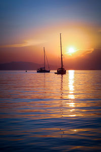 Silhouette sailboat sailing on sea against romantic sky at sunset