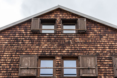 Weathered and faded wooden shingles - the facade of an alpine house. open windows and shutters.