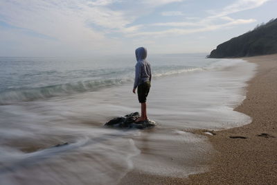 Rear view of man standing at beach against sky