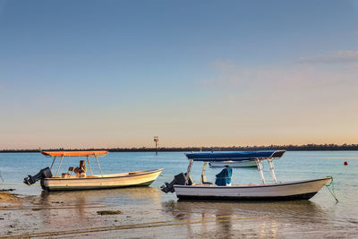 Boats moored in sea against sky during sunset