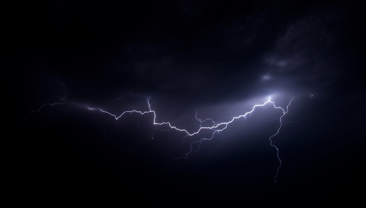 LOW ANGLE VIEW OF LIGHTNING IN SKY OVER SILHOUETTE OF PEOPLE