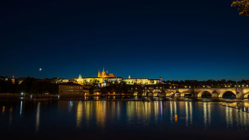 Illuminated buildings by river against sky at night