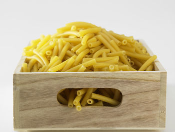 Close-up of raw pasta in crate against white background