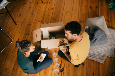 High angle view of couple removing glasses from box in living room at new home