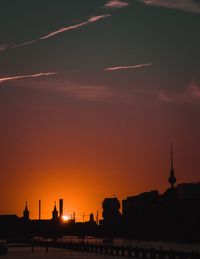 Silhouette buildings in town against sky at sunset