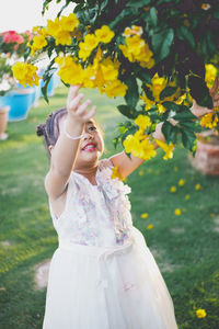 Girl picking yellow flowers on branches at park