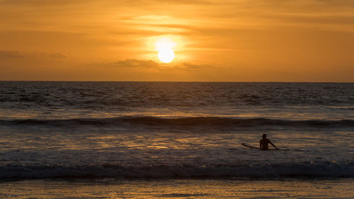 Silhouette man on sea against orange sky during sunset