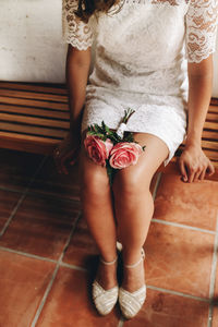 Low section of bride with flower sitting on bench
