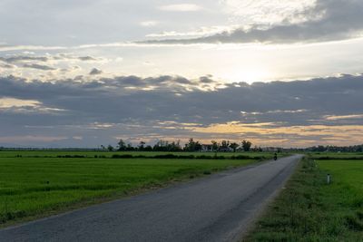 Empty road amidst field against sky during sunset