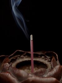 Close-up of incense stick emitting smoke against black background