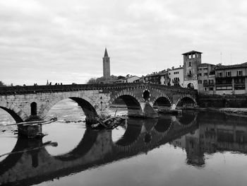 Arch bridge over river by buildings against sky in city