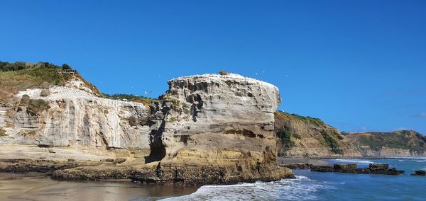 Rock formations by sea against blue sky