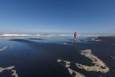 Rear view of girl walking at beach against blue sky