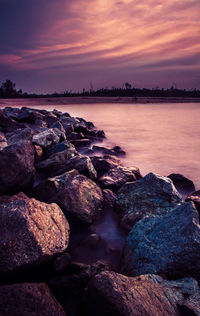 Rocks in sea against sky during sunset