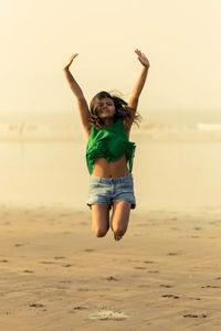 Full length of smiling young woman jumping on beach