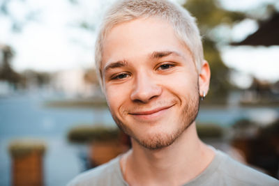 Handsome young man with blond short cut hairstyle smiling over city urban background outdoor. 