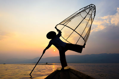 Silhouette man fishing in sea against sky during sunset