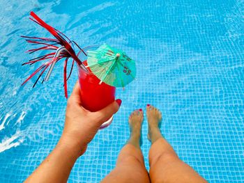 Low section of woman holding drink while sitting by swimming pool