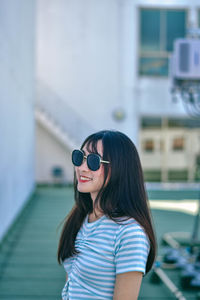 Cheerful young woman wearing sunglasses standing against building