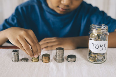 Midsection of boy putting coins in jar on table