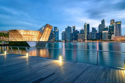 Illuminated buildings by river against sky at dusk