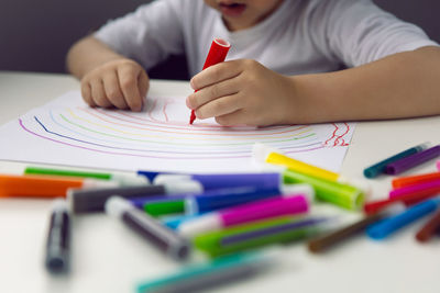 Artist is a boy child sitting at a table at home and drawing with markers on a white sheet