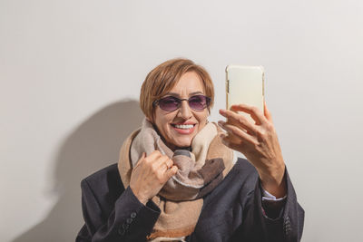 Portrait of young woman using mobile phone against wall