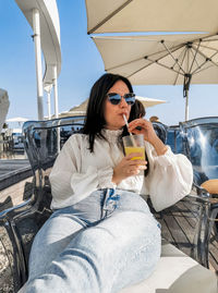 Portrait of beautiful and stylish young woman drinking cold drink in bar on sea shore.