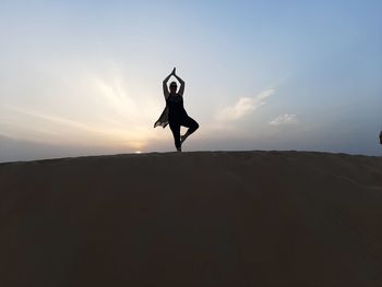 Silhouette woman with arms raised against sky during sunset