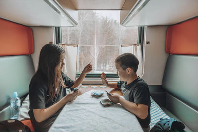 Sibling bonding, in train compartment brother and sister play card game, winter landscape in window