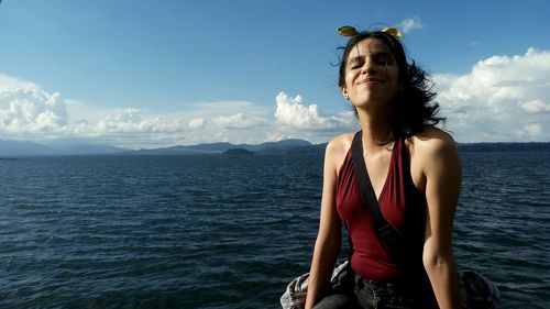 Young woman sitting by sea against sky