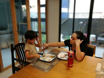 Mother feeding son while sitting at dining table